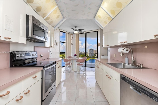 kitchen with light tile patterned flooring, sink, white cabinetry, stainless steel appliances, and a wall of windows