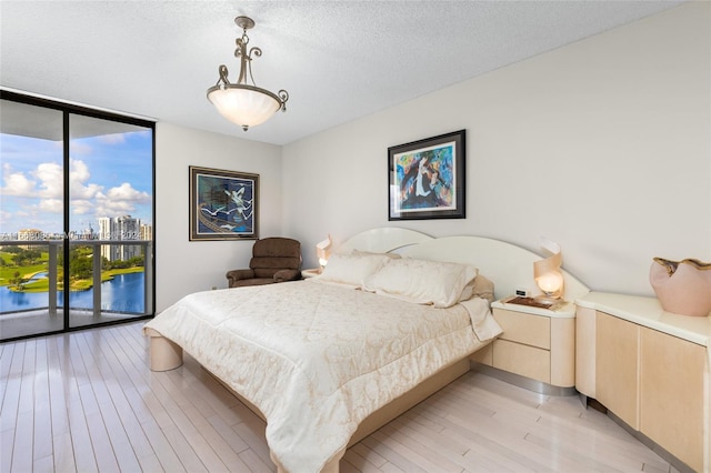 bedroom with access to exterior, multiple windows, expansive windows, and light hardwood / wood-style floors