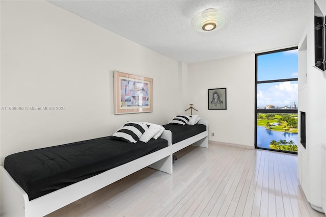 bedroom featuring a textured ceiling, floor to ceiling windows, hardwood / wood-style floors, and a water view