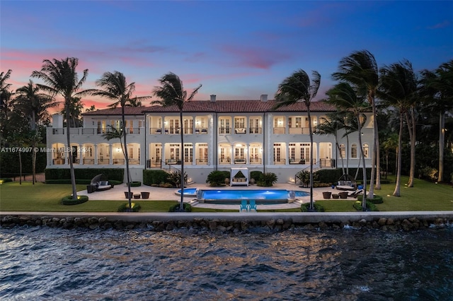 33 Arvida Pkwy, Coral Gables, FL 33156 - back of house at dusk with a patio area, a tile roof, an outdoor pool, a lawn, and a balcony