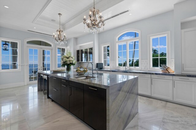 33 Arvida Pkwy, Coral Gables, FL 33156 - kitchen with a sink, a chandelier, an island with sink, french doors, and a tray ceiling