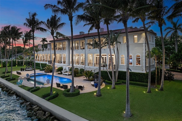 33 Arvida Pkwy, Coral Gables, FL 33156 - back of house at dusk with a patio, a balcony, a yard, a pool with connected hot tub, and stucco siding