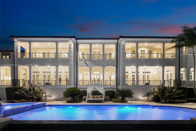 back house at dusk with a pool with hot tub and a balcony