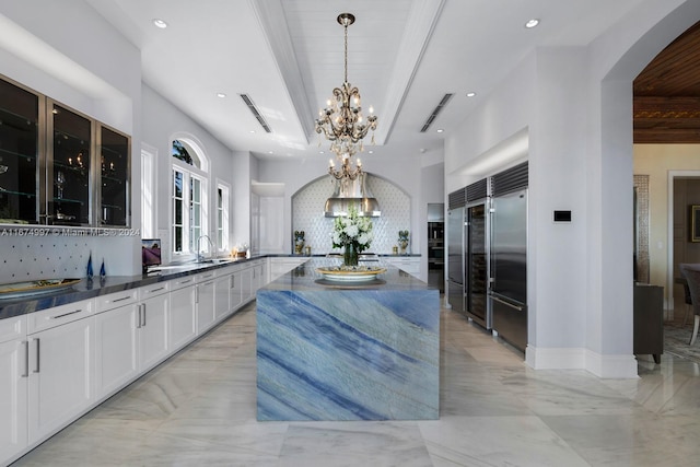 kitchen featuring white cabinets, stainless steel built in refrigerator, tasteful backsplash, hanging light fixtures, and sink