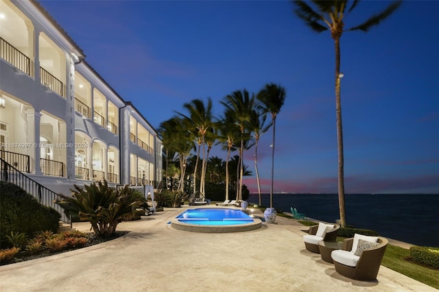 pool at dusk featuring a water view, a patio, and a hot tub