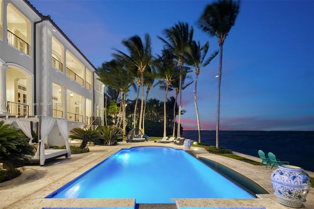 pool at dusk with a patio area and a water view