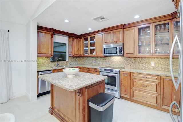 kitchen with decorative backsplash, a kitchen island, appliances with stainless steel finishes, light stone countertops, and sink