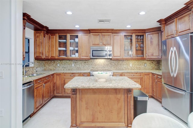 kitchen with light stone countertops, sink, a kitchen island, backsplash, and stainless steel appliances