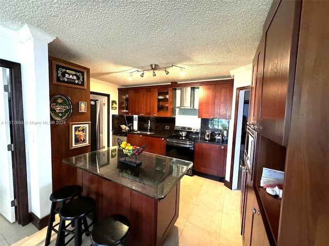 kitchen with a kitchen breakfast bar, stainless steel appliances, sink, wall chimney range hood, and a center island