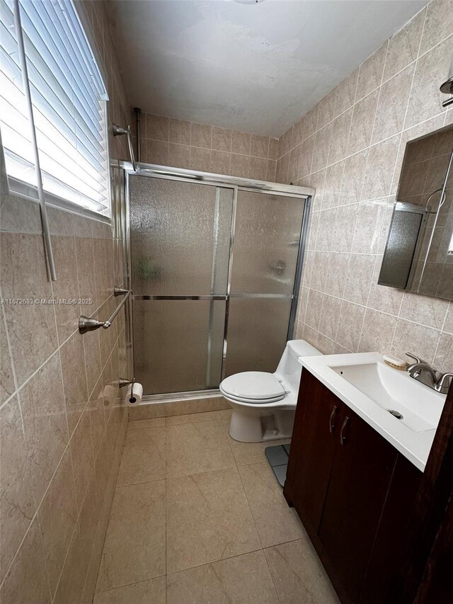 bathroom featuring vanity, a shower with shower door, tile walls, and toilet