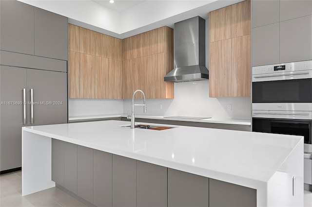 kitchen featuring wall chimney range hood, a large island with sink, black electric stovetop, double oven, and sink