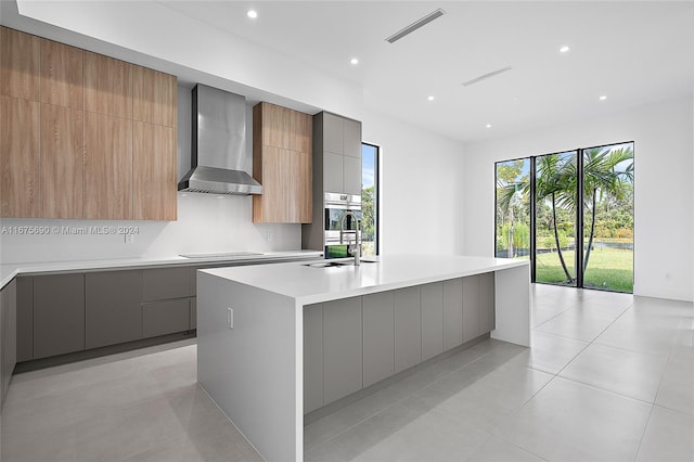 kitchen with a large island with sink, sink, wall chimney range hood, and a healthy amount of sunlight