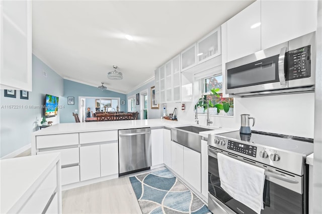 kitchen featuring light hardwood / wood-style flooring, vaulted ceiling, stainless steel appliances, kitchen peninsula, and white cabinets