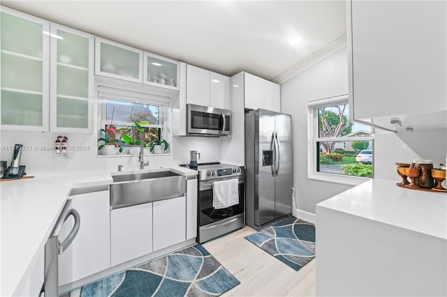 kitchen featuring light wood-type flooring, stainless steel appliances, sink, white cabinetry, and ornamental molding