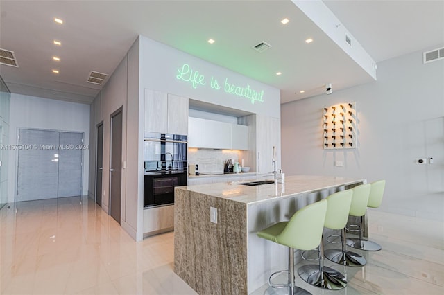 kitchen featuring light stone countertops, sink, a center island with sink, white cabinets, and a breakfast bar area