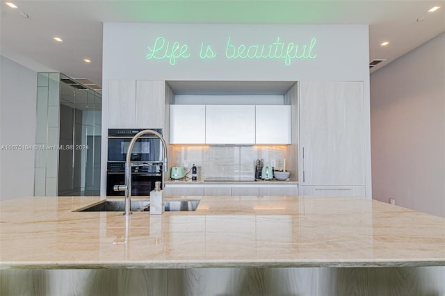 kitchen with black appliances, sink, decorative backsplash, light stone counters, and white cabinetry