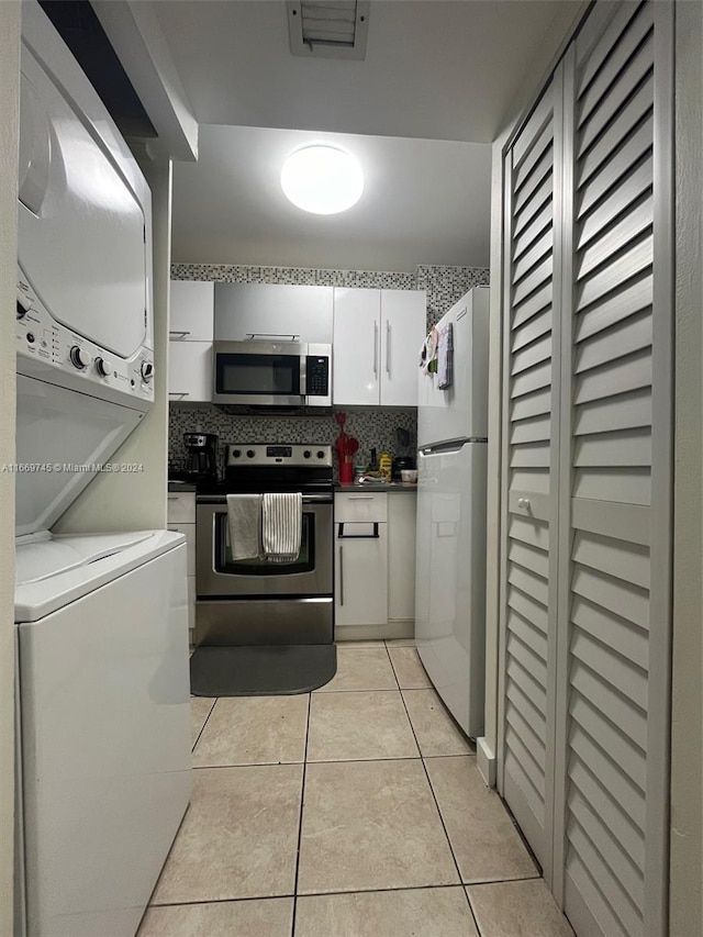 kitchen featuring stacked washer and clothes dryer, backsplash, white cabinets, appliances with stainless steel finishes, and light tile patterned floors