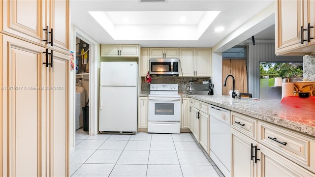 kitchen with white appliances, a tray ceiling, light stone counters, and cream cabinetry