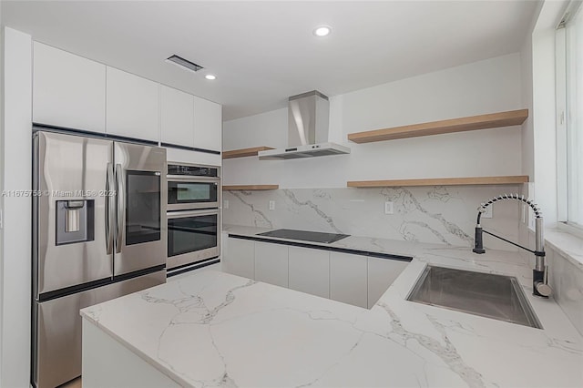 kitchen with wall chimney exhaust hood, white cabinetry, appliances with stainless steel finishes, light stone countertops, and decorative backsplash