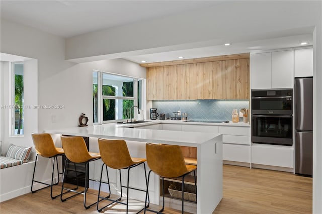 kitchen with kitchen peninsula, white cabinets, black appliances, and light wood-type flooring