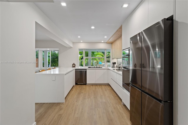 kitchen featuring kitchen peninsula, stainless steel appliances, sink, white cabinets, and light hardwood / wood-style floors