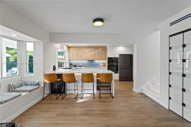 kitchen featuring sink, light hardwood / wood-style flooring, a kitchen bar, kitchen peninsula, and stainless steel refrigerator