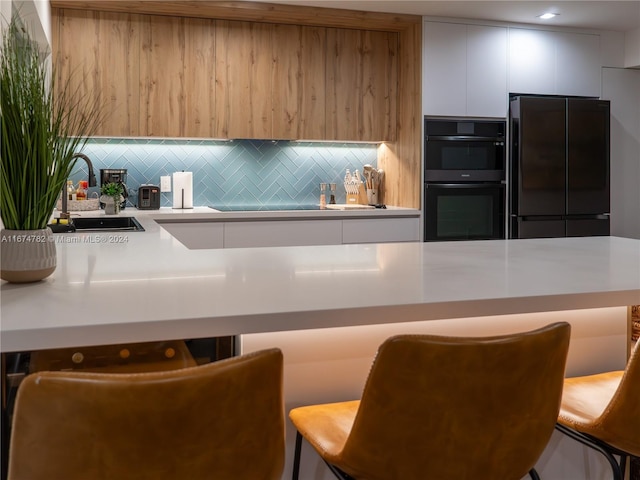 kitchen with white cabinets, sink, black double oven, decorative backsplash, and stainless steel refrigerator