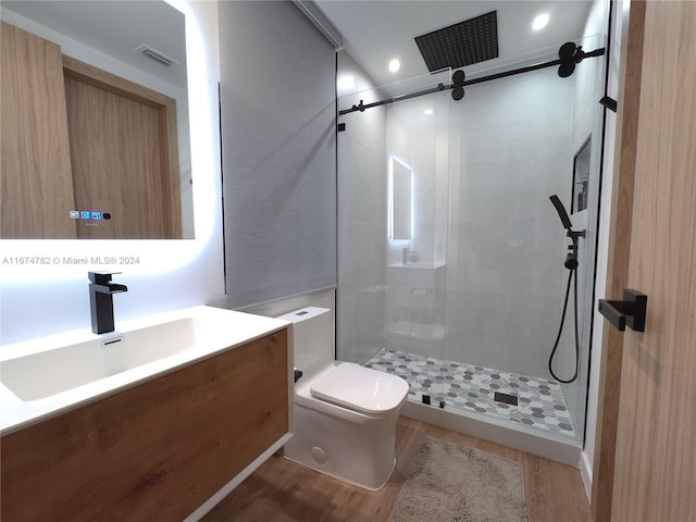 bathroom featuring tiled shower, vanity, wood-type flooring, and toilet