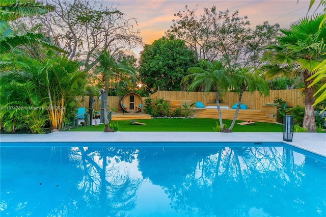 pool at dusk featuring a yard and a wooden deck