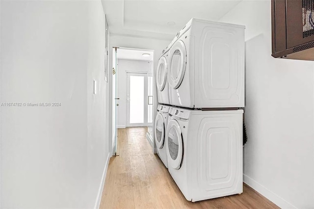 laundry area featuring cabinets, stacked washing maching and dryer, and light hardwood / wood-style floors