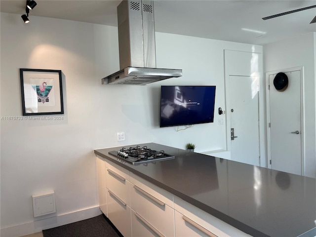 kitchen with ceiling fan, white cabinetry, wall chimney exhaust hood, and stainless steel gas cooktop