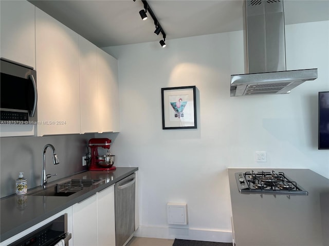 kitchen featuring sink, wall chimney range hood, track lighting, white cabinets, and appliances with stainless steel finishes