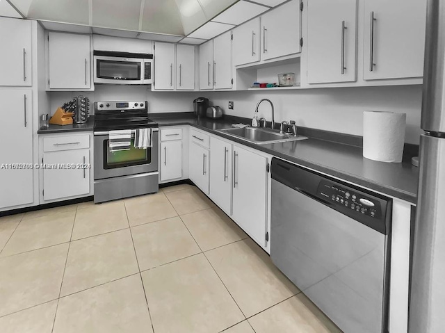 kitchen with appliances with stainless steel finishes, light tile patterned floors, white cabinetry, and sink