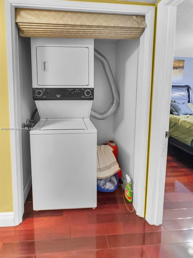 clothes washing area featuring stacked washer / drying machine and dark wood-type flooring