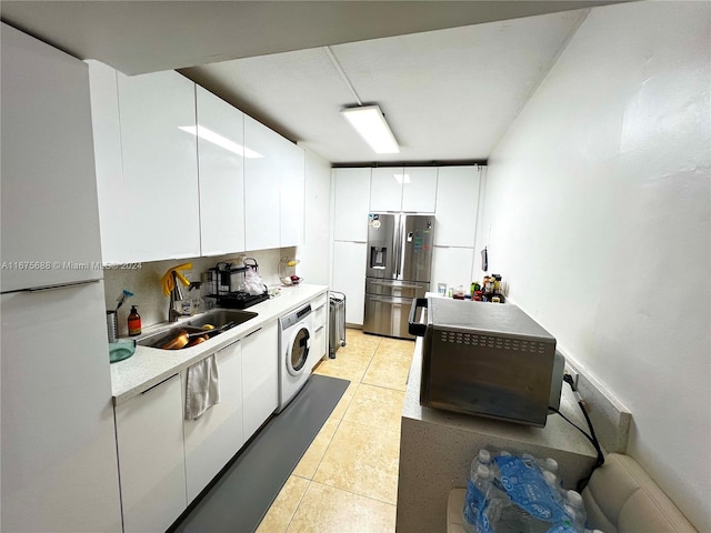 kitchen with light tile patterned flooring, sink, washer / dryer, white cabinets, and stainless steel fridge with ice dispenser