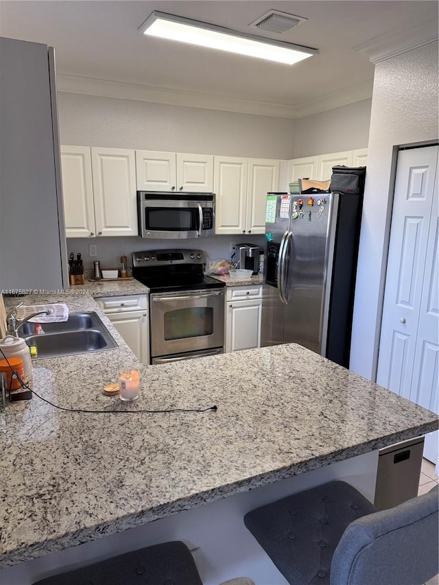 kitchen featuring ornamental molding, sink, a kitchen bar, white cabinetry, and appliances with stainless steel finishes