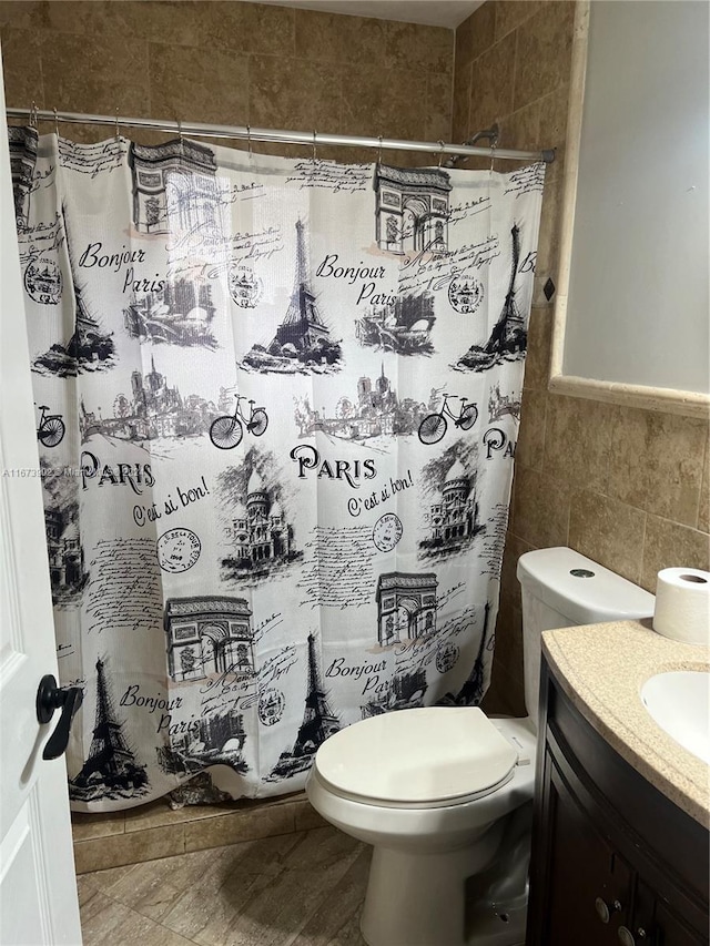 bathroom featuring walk in shower, vanity, toilet, and tile walls