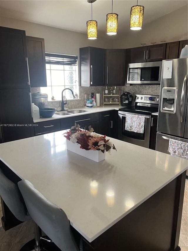 kitchen with hanging light fixtures, sink, backsplash, appliances with stainless steel finishes, and a breakfast bar