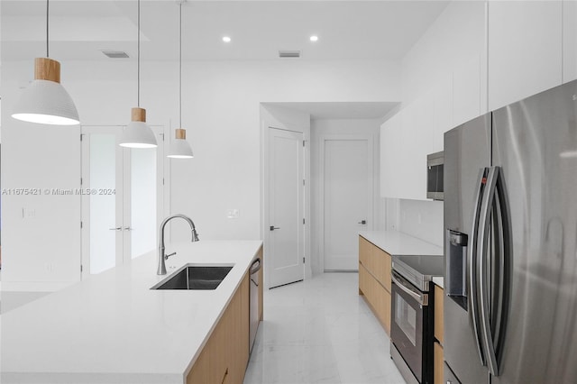 kitchen with a large island with sink, sink, stainless steel appliances, decorative light fixtures, and white cabinets