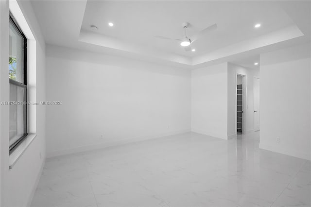 empty room with ceiling fan and a tray ceiling