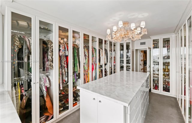 spacious closet featuring an inviting chandelier and dark colored carpet