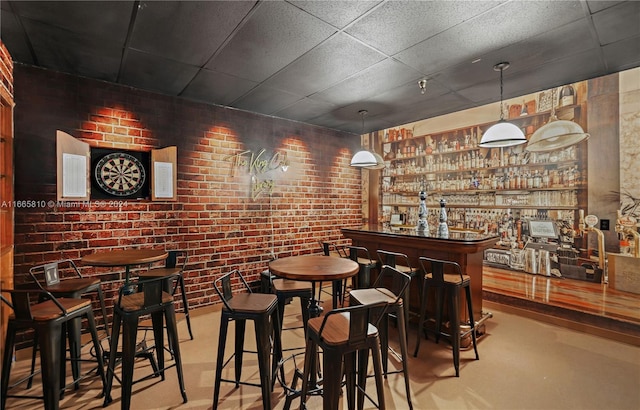 bar featuring a drop ceiling, pendant lighting, brick wall, and concrete flooring