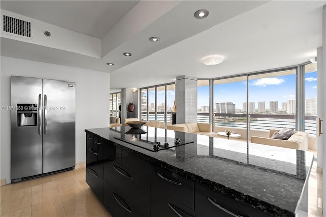 kitchen featuring black electric cooktop, a large island, dark stone counters, and stainless steel refrigerator with ice dispenser