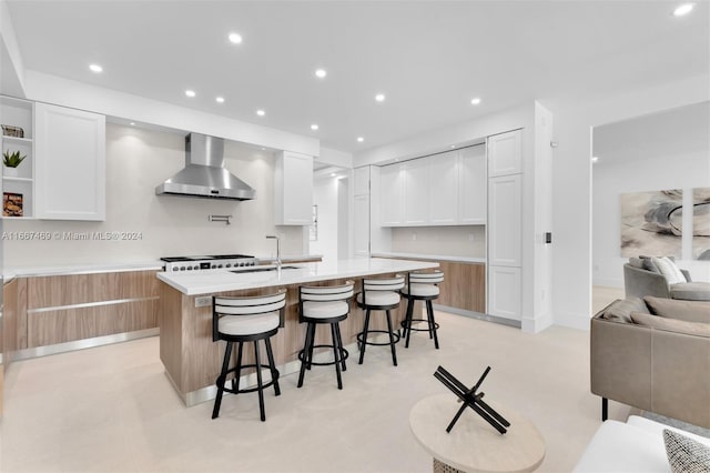 kitchen with a center island with sink, wall chimney range hood, and white cabinetry