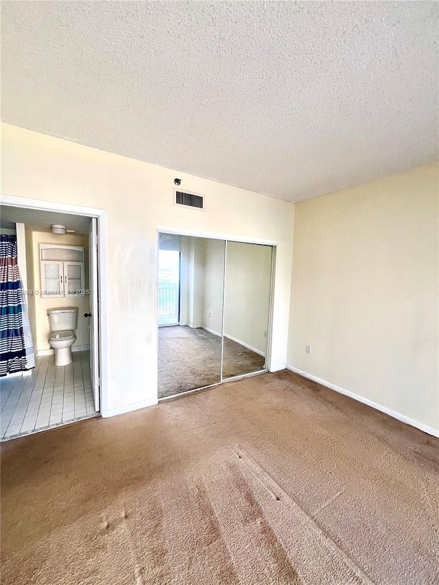 unfurnished bedroom featuring carpet, ensuite bathroom, a closet, and a textured ceiling