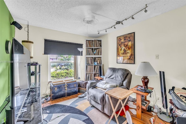 living area featuring ceiling fan, hardwood / wood-style flooring, track lighting, and a textured ceiling