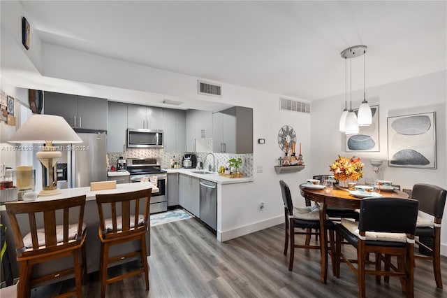 kitchen featuring decorative backsplash, hardwood / wood-style floors, stainless steel appliances, sink, and pendant lighting