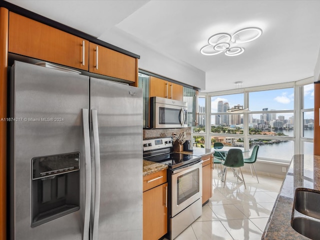 kitchen with a water view, dark stone counters, appliances with stainless steel finishes, light tile patterned floors, and backsplash