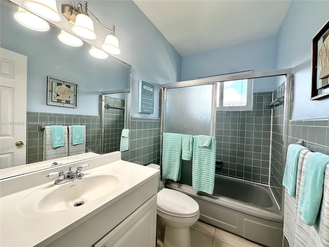 full bathroom featuring shower / bath combination with glass door, toilet, tile walls, vanity, and tile patterned flooring