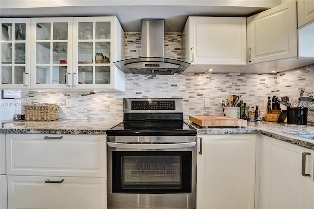 kitchen with stainless steel electric stove, white cabinets, wall chimney range hood, tasteful backsplash, and light stone counters